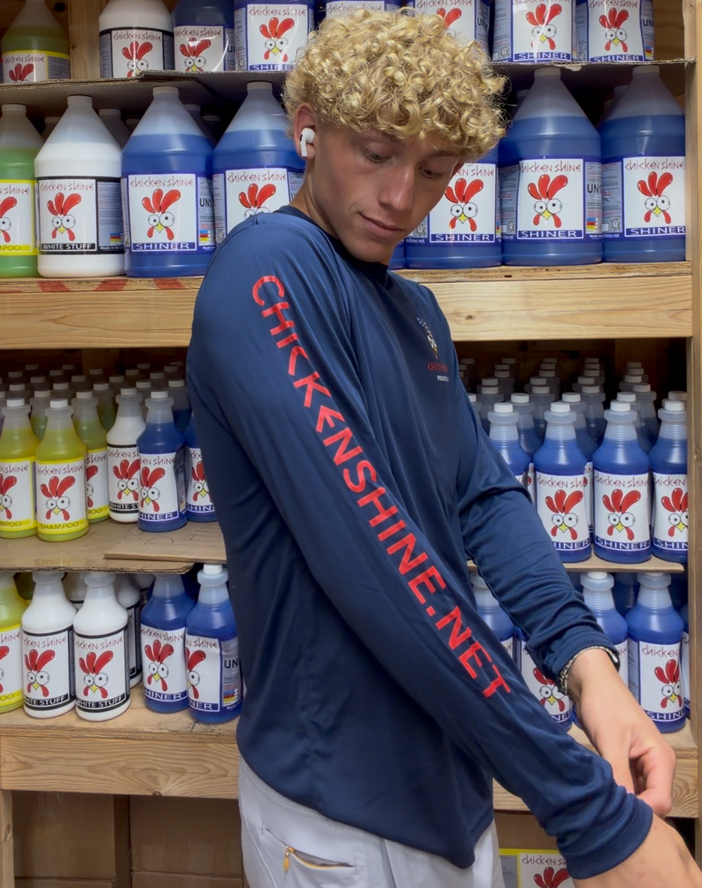 Person wearing a blue shirt with 'Chickenshine.net' text in a store with shelves of bottles.