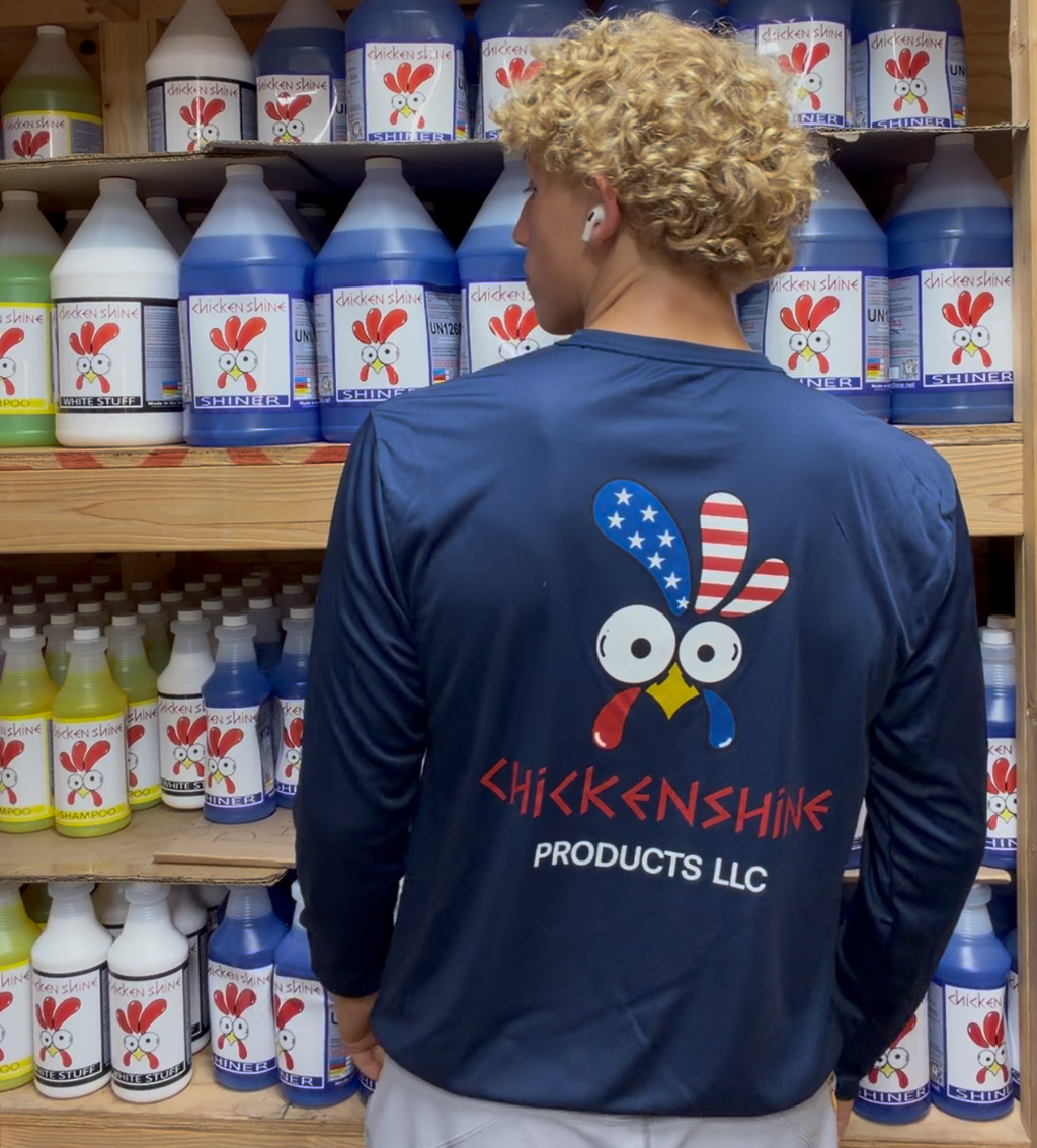 Person wearing a blue shirt with a logo and text standing in front of shelves stocked with various bottles.